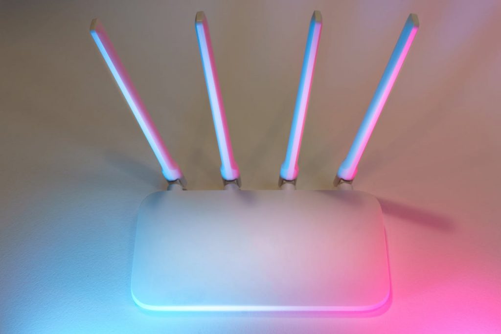 pexels-photo-29711663 Sleek white wireless router with four antennas emitting soft blue and pink light.