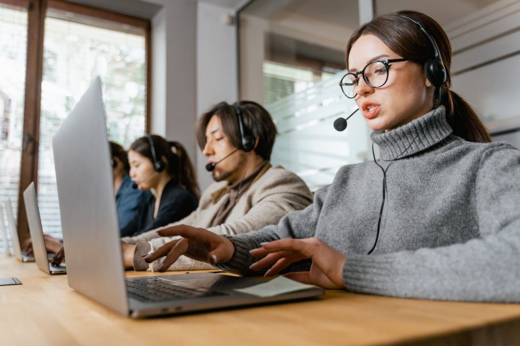 pexels-photo-7709181 Four call center employees working with headsets and laptops in a modern office setting.